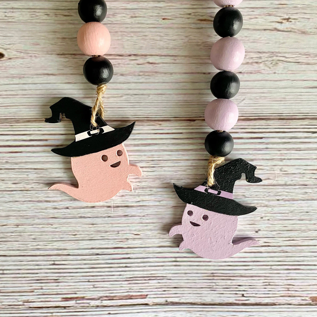 ghosts in witch hats on a beaded garland one is pink one is lavender