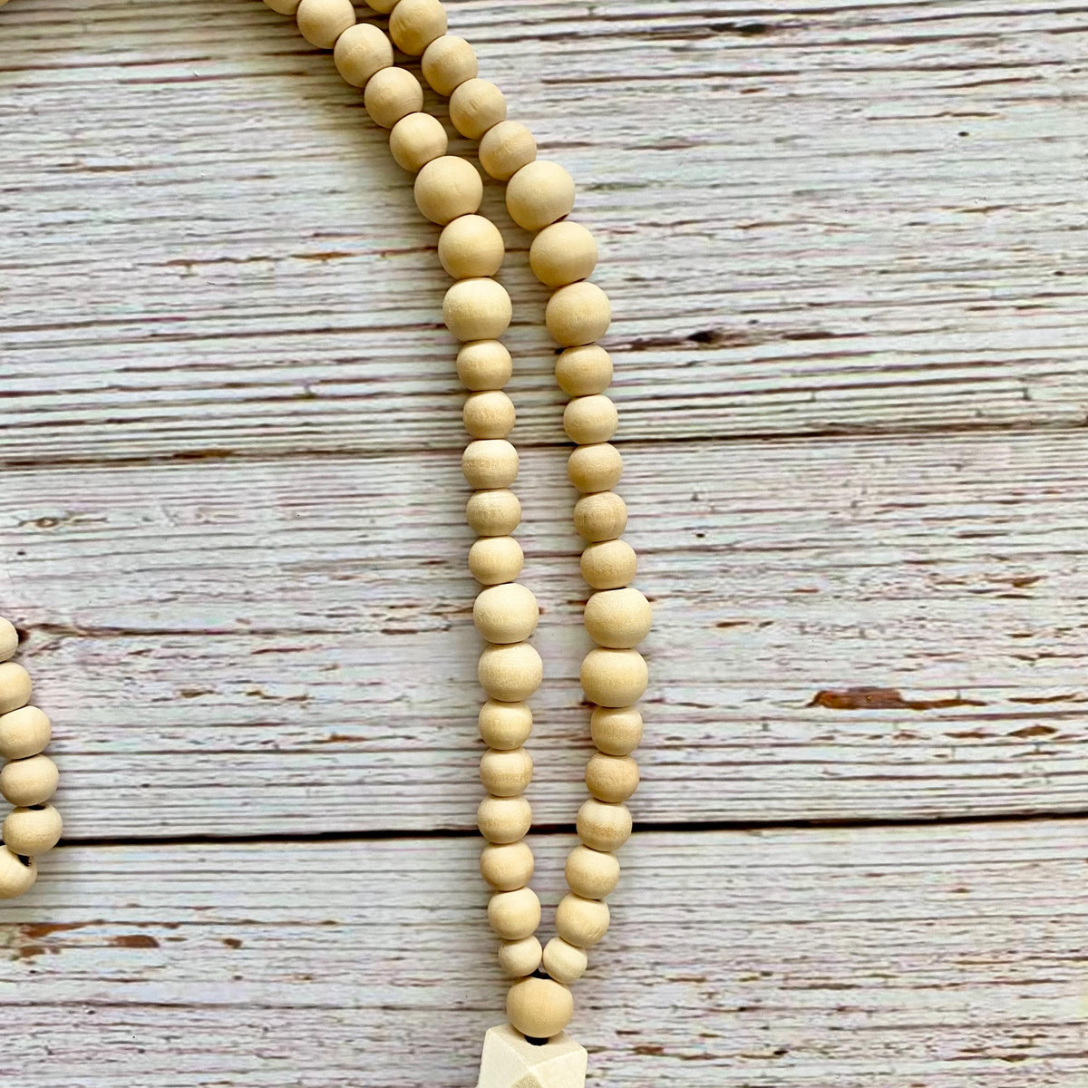 A close-up of a light natural wood bead necklace laid on a weathered whitewashed wooden surface.