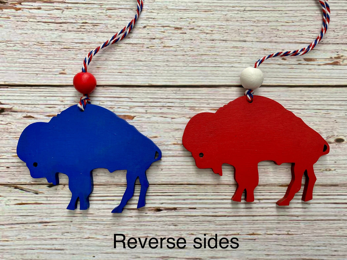Two buffalo-shaped hanging ornaments shown on a whitewashed wood background, one blue and one red, each with a string and bead. Text at the bottom reads 'Reverse sides'.