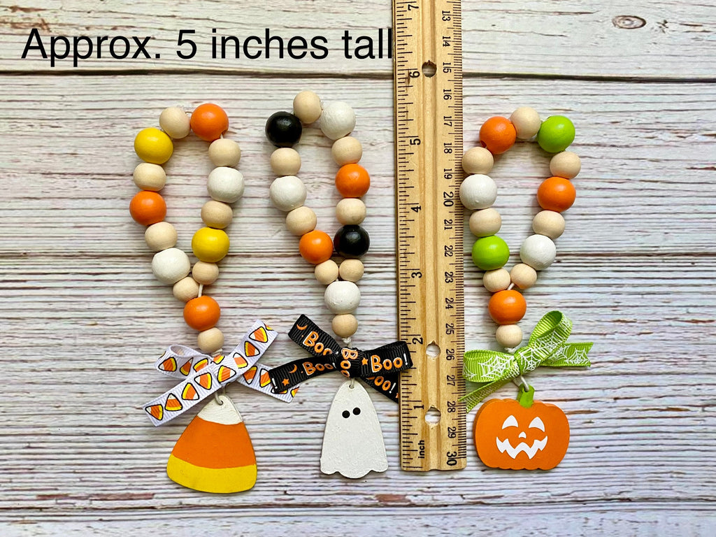 Three Halloween-themed wooden bead garlands displayed on a whitewashed wood background with a wooden ruler for scale and text reading 'Approx. 5 inches tall.