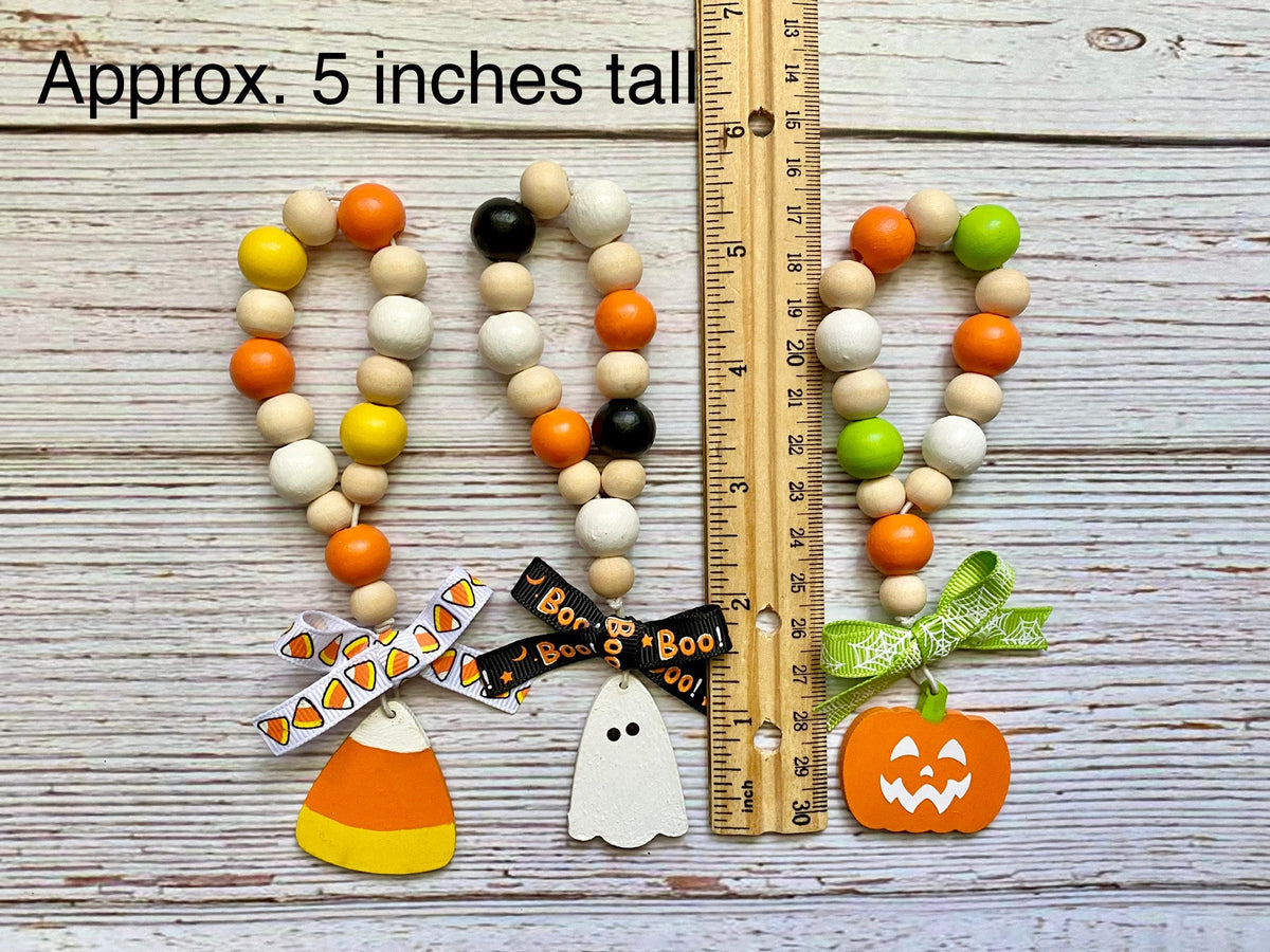 Three Halloween-themed wooden bead garlands displayed on a whitewashed wood background with a wooden ruler for scale and text reading 'Approx. 5 inches tall.