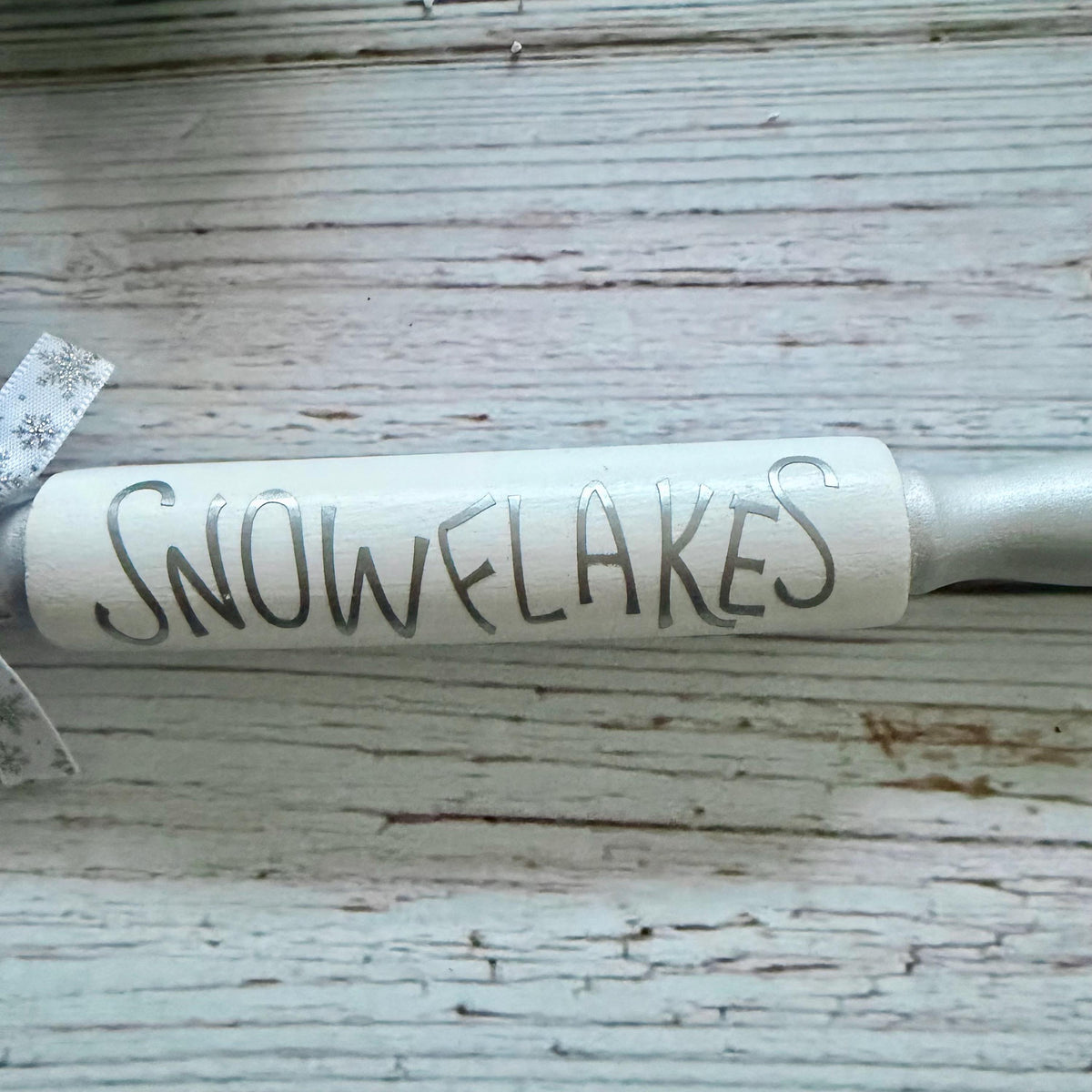 A close-up of a cylindrical product with the word "SNOWFLAKES" written across it in dark lettering, resting on a distressed white wood surface.