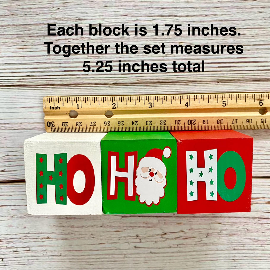 Three wooden HOHO blocks with festive holiday lettering and a Santa Claus face, shown with a wooden ruler and text stating each block is 1.75 inches and the set measures 5.