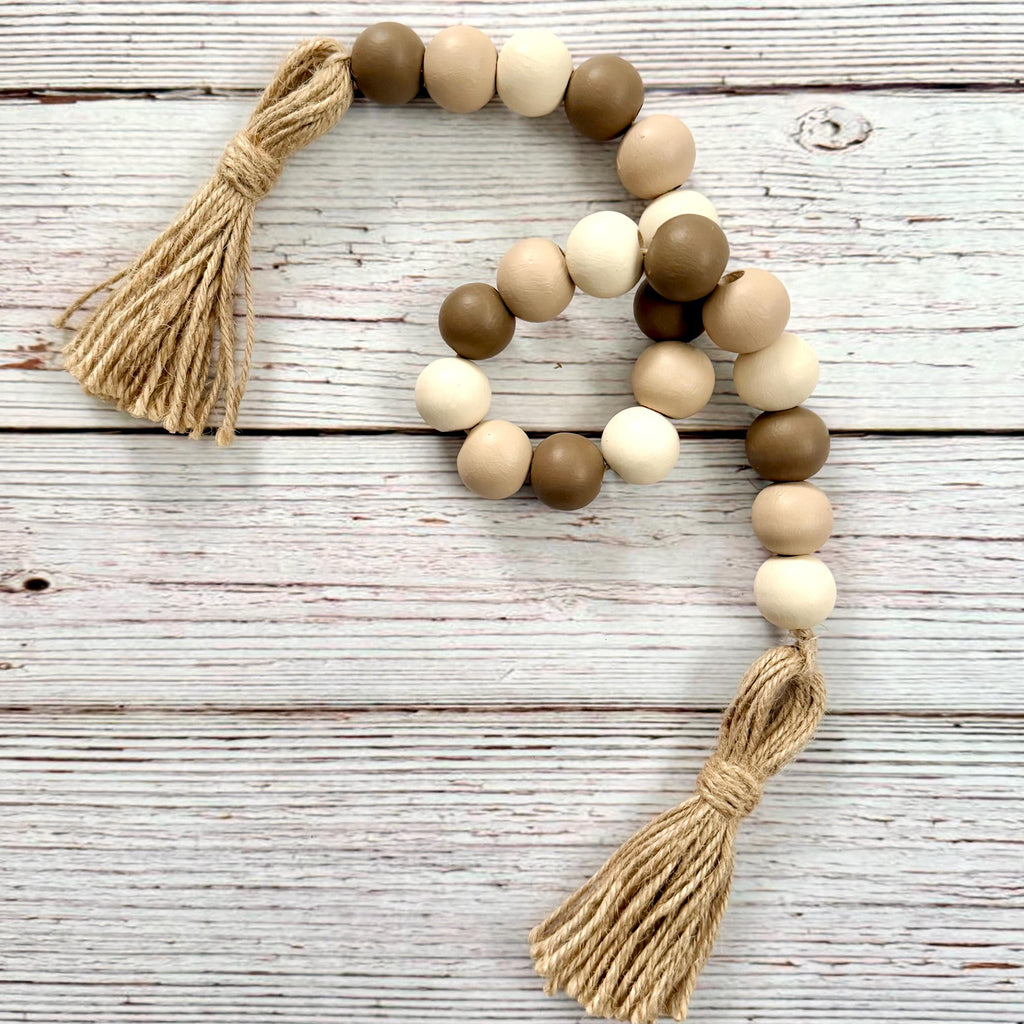 a wood bead garland in shades of brown with tassels on a whitewashed wood background