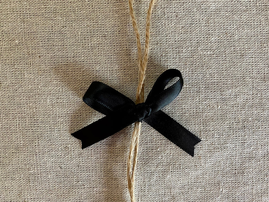 A small black satin ribbon bow tied around a natural jute twine bundle, placed on a textured beige linen fabric background.