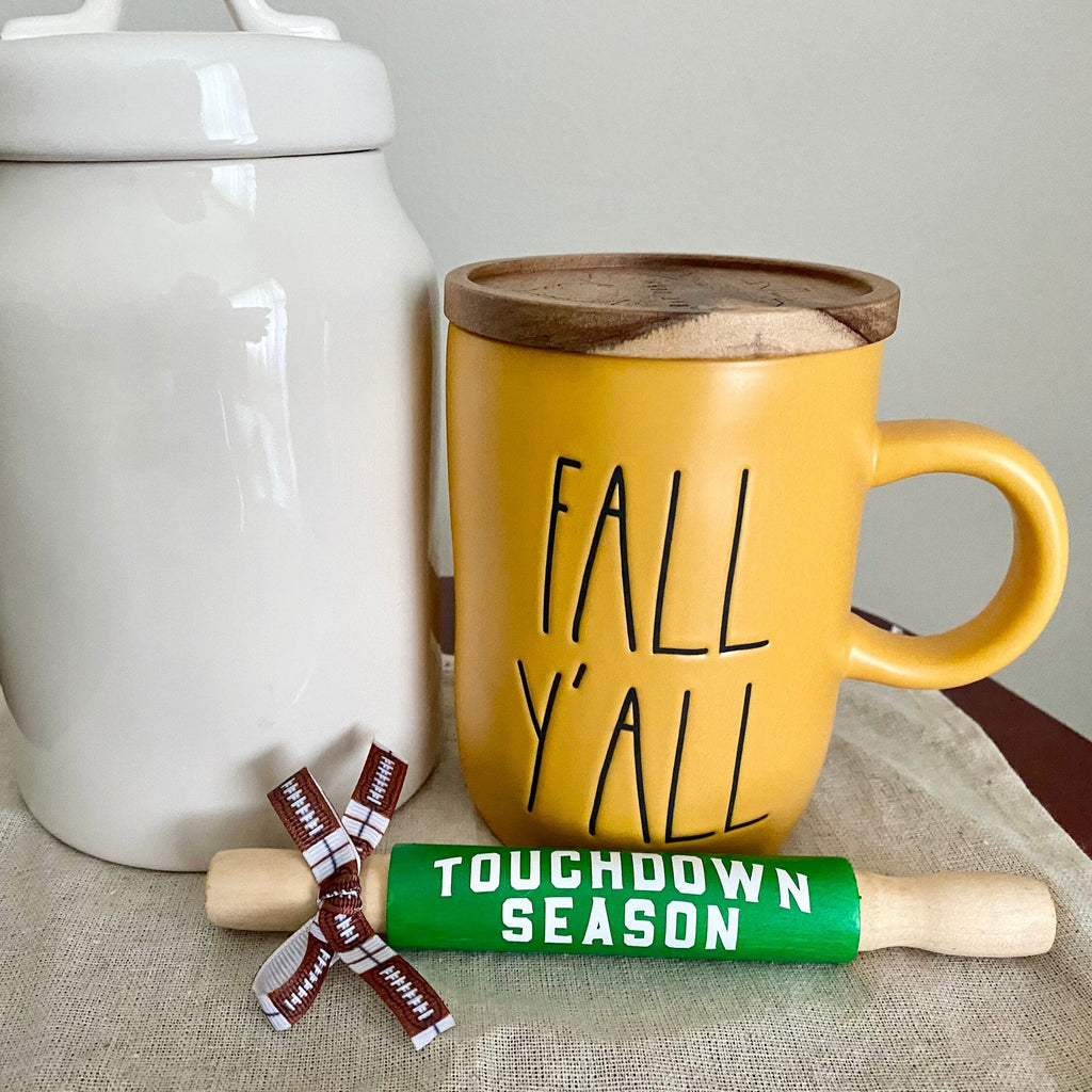 a white canister and yellow mug with fall yall behind a mini rolling pin in bright green that reads touchdown season in white.  tied with a football print bow on the handle