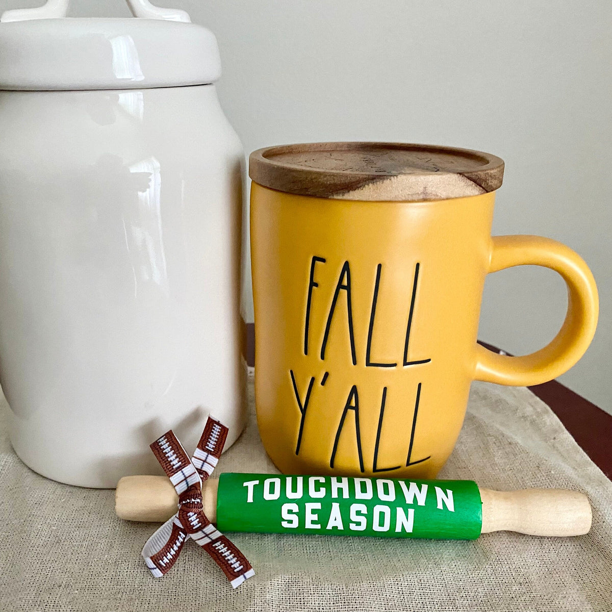 a white canister and yellow mug with fall yall behind a mini rolling pin in bright green that reads touchdown season in white.  tied with a football print bow on the handle