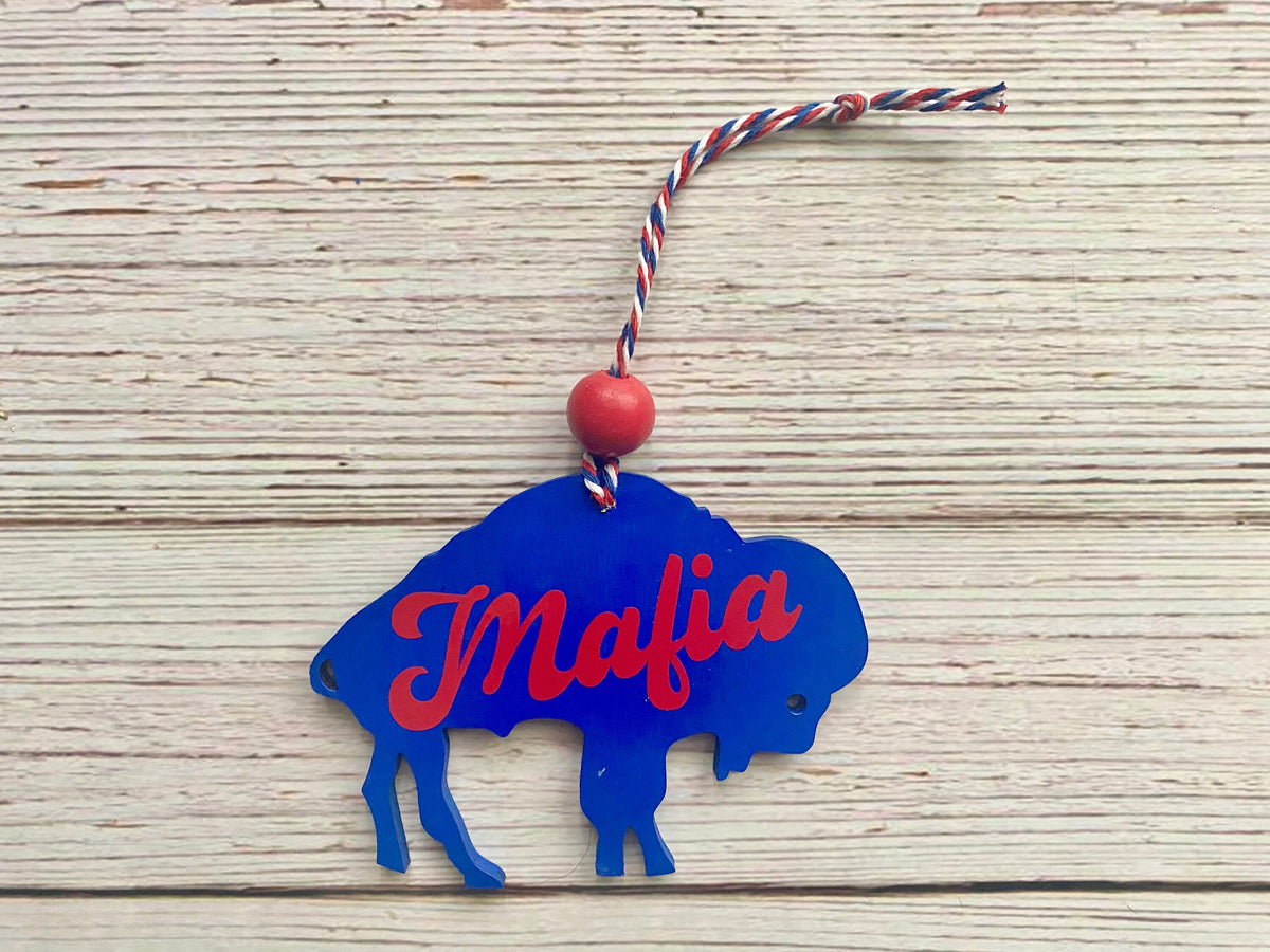 A blue buffalo-shaped hanging ornament with the word 'Mafia' in red script across the front, attached to a red, white, and blue string with a red bead, shown on a light wood background.