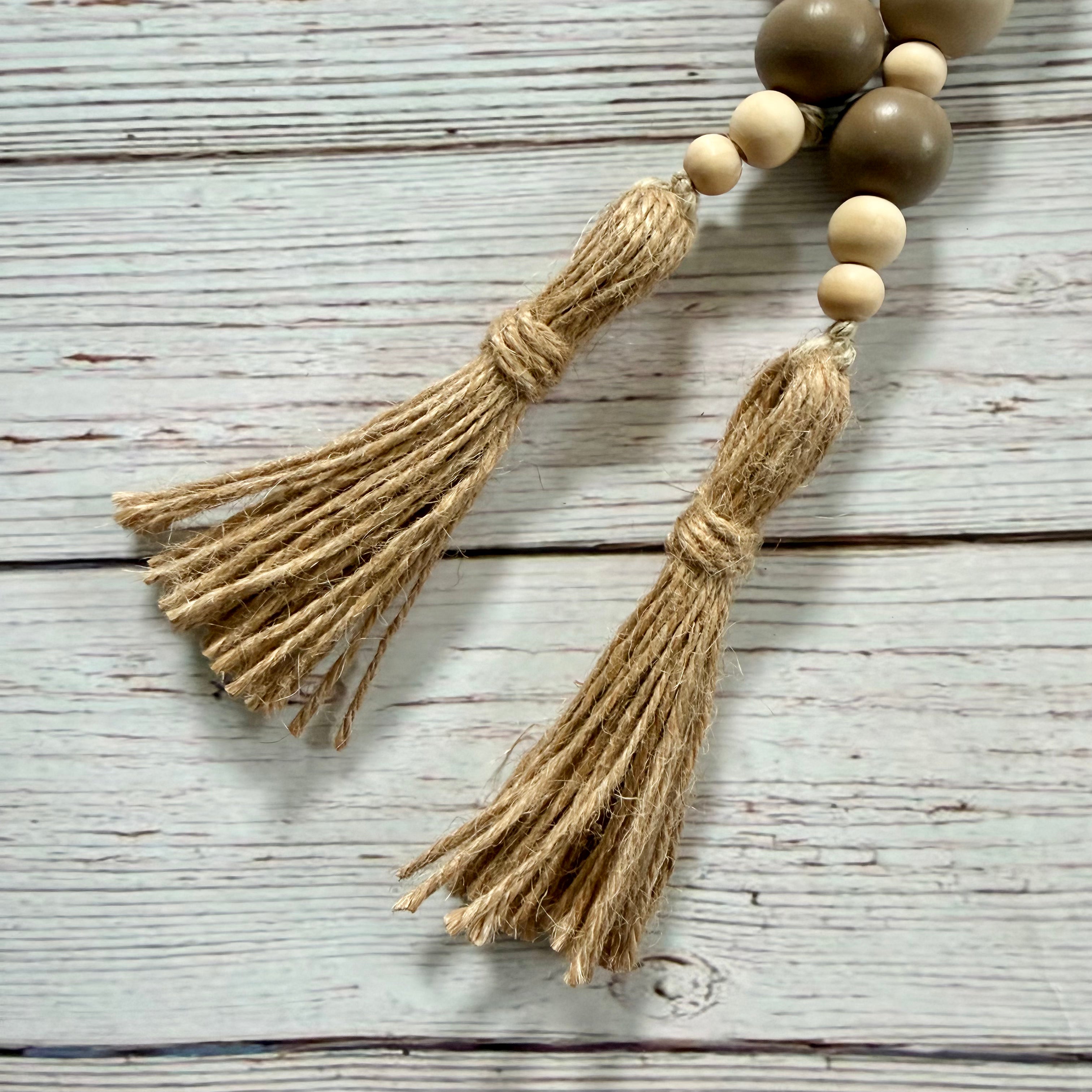 Natural jute tassel garland with wooden beads in light beige and medium brown, laid on a whitewashed wood plank surface.