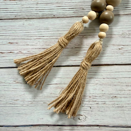 Natural jute tassel garland with wooden beads in light beige and medium brown, laid on a whitewashed wood plank surface.