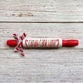 A red and white wooden rolling pin with 'candy cane lane' written on the center in red script, tied with a red and white striped ribbon, on a rustic white wood background.