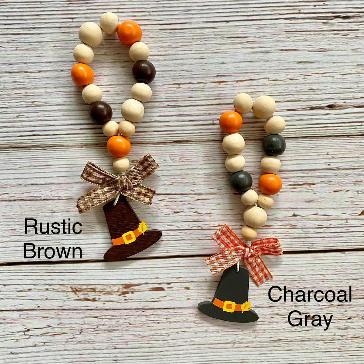 Two beaded witch hats displayed on a whitewashed wood background, labeled 'Rustic Brown' and 'Charcoal Gray.' Each hat is made from wooden beads in natural cream, orange, and dark brown/gray, with a small bow and painted witch hat charm.