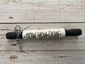 A novelty rolling pin with a white body, black handles, and the phrase 'HOW YOU DOIN'' printed on it in black with small colored dots, tied with a black-and-white string, on a rustic white wood background.