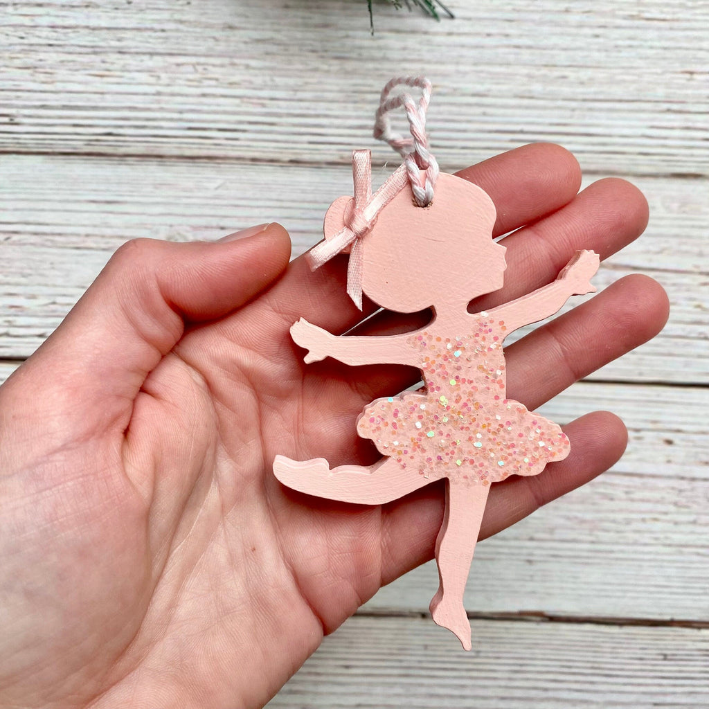 hand holding a light pink ballerina wood ornament with a glitter dress and bow in her hair