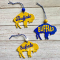 Three buffalo-shaped hanging ornaments on a whitewashed wood background. Two ornaments are yellow with blue 'Buffalo' lettering, and one is blue with yellow 'BUFFALO' lettering.