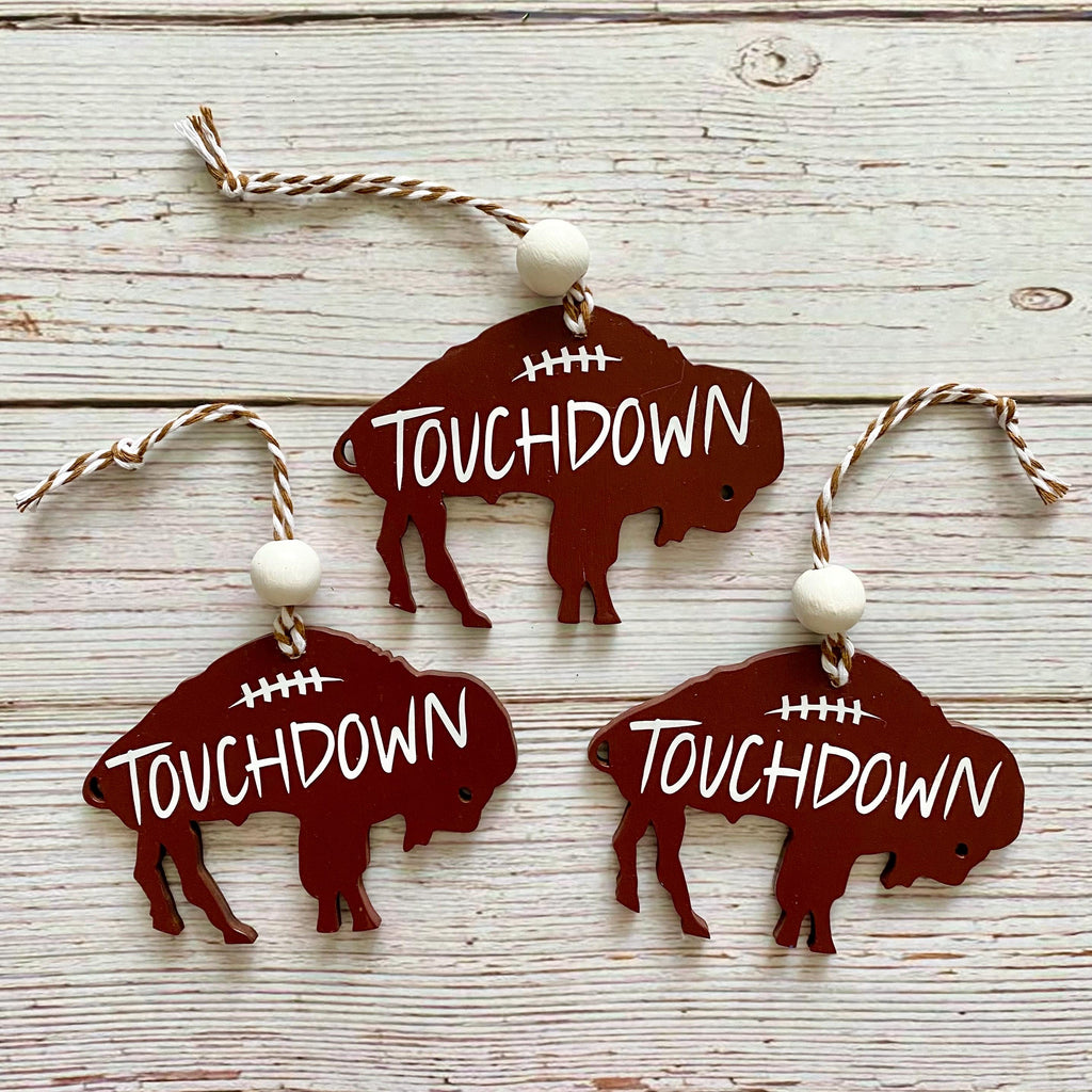 Three buffalo-shaped wooden ornaments with 'TOUCHDOWN' text and white beads, displayed on a whitewashed wood background.