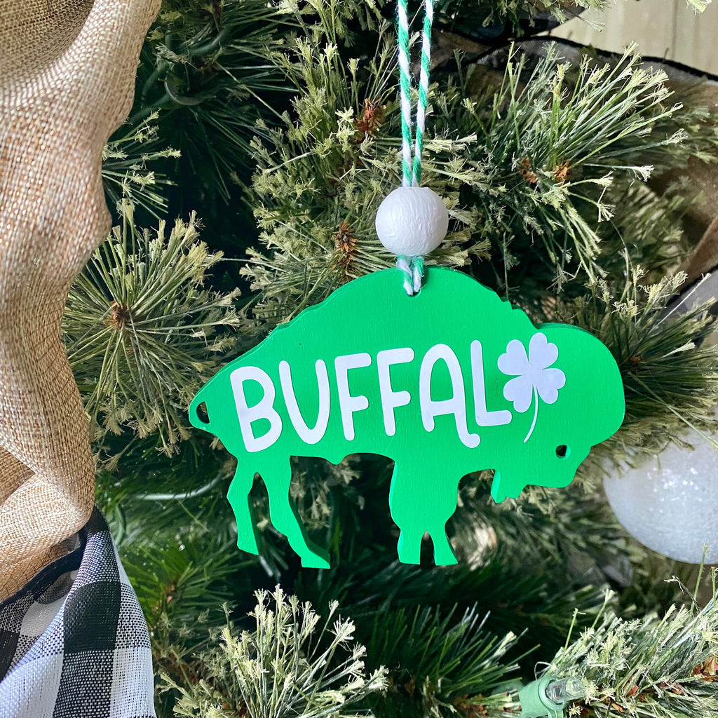 A bright green St. Patrick's Day buffalo ornament hanging from a string on a decorated Christmas tree.