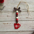 A rustic Christmas ornament shaped like a red mug with a white snowflake, hanging from a brown polka-dot ribbon bow and a string of red, white, and brown beads on a whitewashed wooden background.