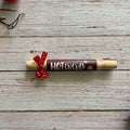 A wooden hot cocoa holder shaped like a rolling pin, featuring a dark brown center with the words 'HOT cocoa' in white and a red polka-dot ribbon tied around it, displayed on a rustic white wood plank background.