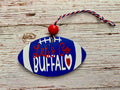 A football-shaped decorative ornament with a blue and white painted finish, white laces, red script text reading 'Let's Go BUFFALO,' a small red heart, and a red-and-white hanging cord, displayed on a rustic wood surface.