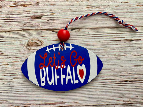 A football-shaped decorative ornament with a blue and white painted finish, white laces, red script text reading 'Let's Go BUFFALO,' a small red heart, and a red-and-white hanging cord, displayed on a rustic wood surface.
